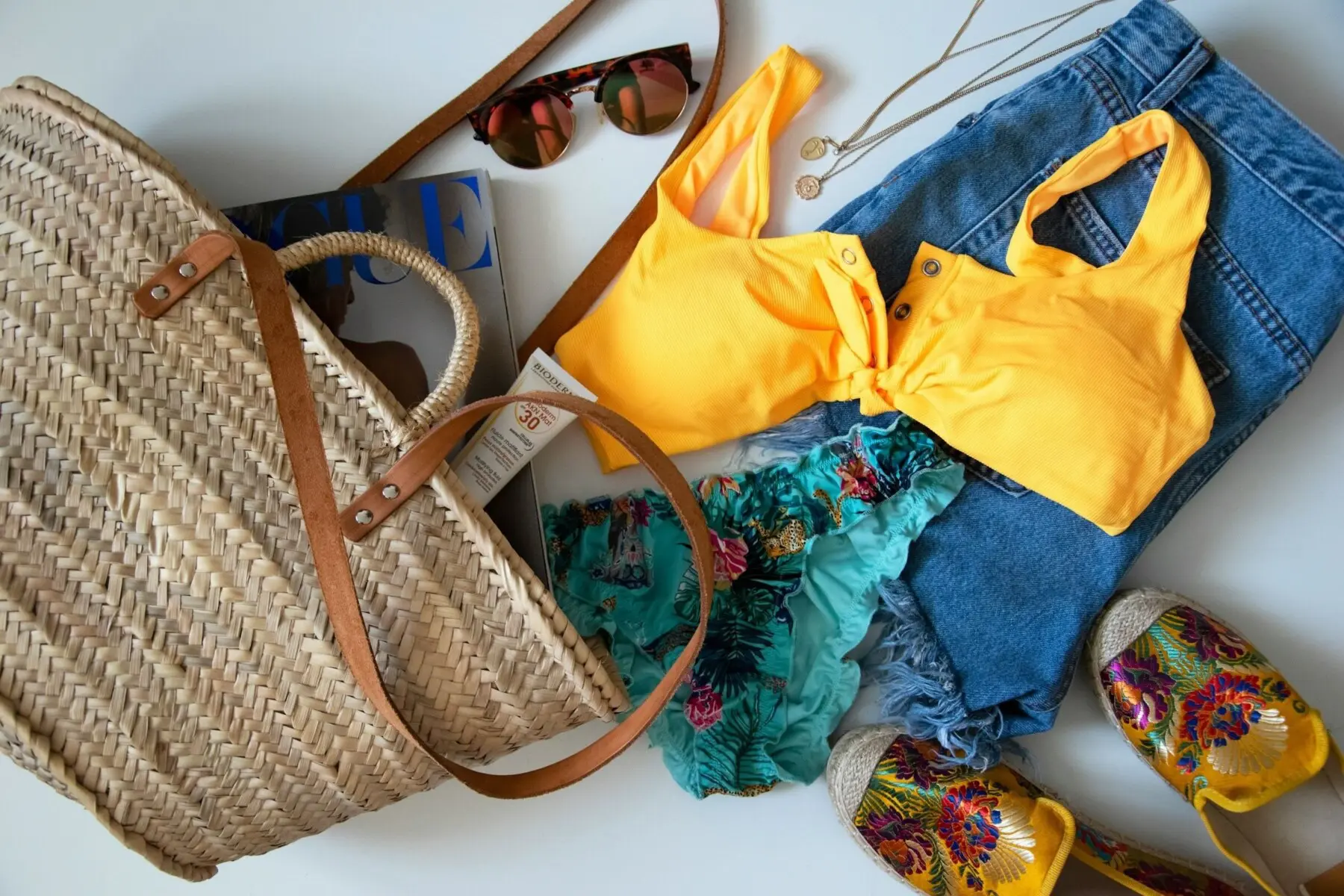 Beach essentials flat lay with straw bag, swimsuit, sunglasses, and sunscreen, for packing for a Siesta Key, Florida vacation, what to pack for Siesta Key checklist