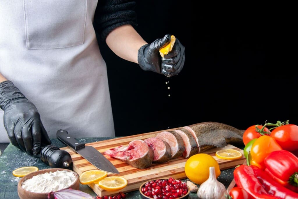 front view chef squeezing lemon raw fish slices knife cutting board vegetables wood serving board kitchen table scaled 1.jpg