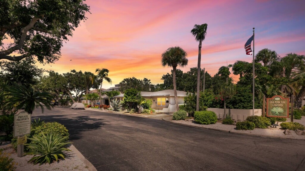 Entrance to Provincial Gardens on Siesta Key at sunset with the community sign and palm-lined drive, ideal for guests booking a beach-to-bay vacation rental.