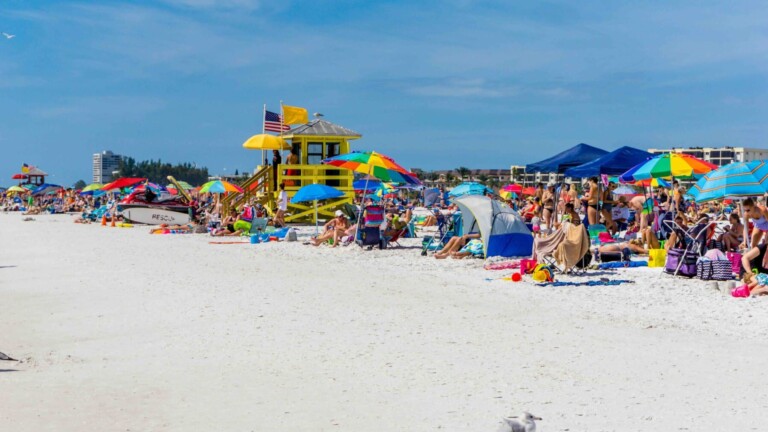 Crowded beach with colorful umbrellas on Siesta Key, Florida during spring break season — what Siesta Key Spring Break crowds feel like