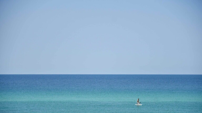 Paddleboarder on calm turquoise Gulf water near Siesta Key, Florida, showing swimming conditions for a Siesta Key water temperature by month guide